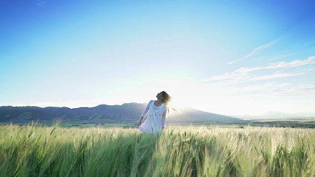 一个年轻女孩在夕阳下的麦田里跳舞。视频素材