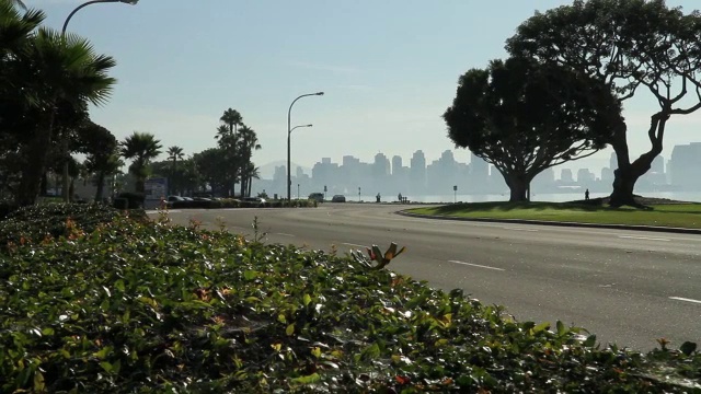 沿滨水区道路行驶的汽车从右向左行驶。圣迭戈城市天际线和海湾在bg。视频素材