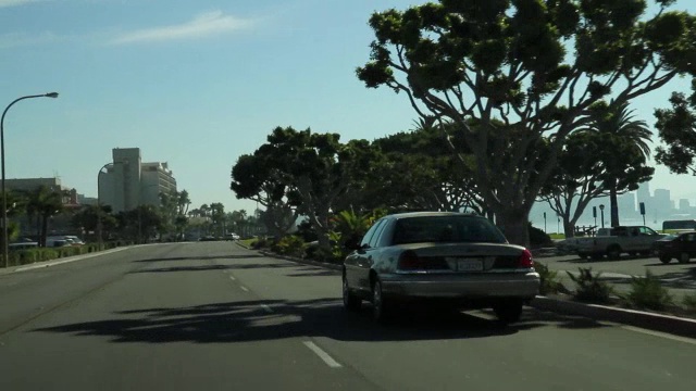 在滨水区道路上行驶的汽车的右前方的广角行驶。圣迭戈城市天际线和海湾在bg。视频素材