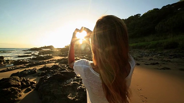 白种人女性框架在海滩上日落成心的形状视频素材