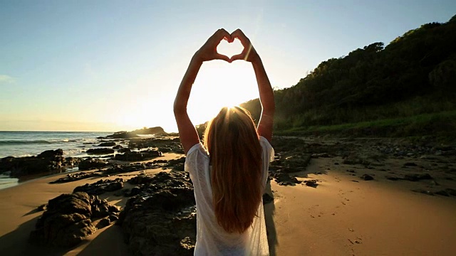 白种人女性框架在海滩上日落成心的形状视频素材