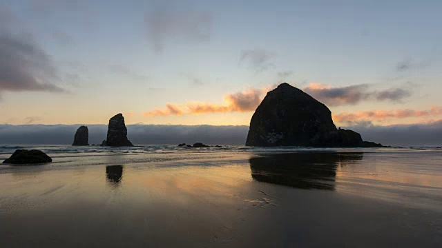 时间流逝低云沿太平洋在Cannon海滩低潮日落到傍晚与美丽的反射干草堆岩石视频素材