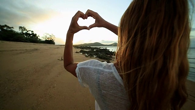 年轻女子把海滩上的夕阳画成心形视频素材