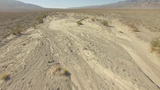 WS AERIAL POV低空飞行，飞越死亡谷的干涸河床和沙漠植被，远处是Tucki山/美国加利福尼亚州视频素材