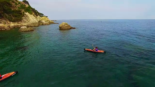 用无人机拍摄的航拍画面，两个女孩在地中海科斯塔布拉瓦的一个田园诗般的地方，清澈清澈的海水中练习划艇。4 k UHD。视频素材