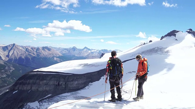 两个年轻的登山运动员走到檐口上，眺望冰川对面的山峰视频素材