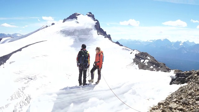 两个年轻的登山运动员走到檐口上，眺望冰川对面的山峰视频素材