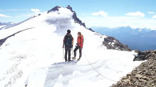 两个年轻的登山运动员走到檐口上，眺望冰川对面的山峰视频素材