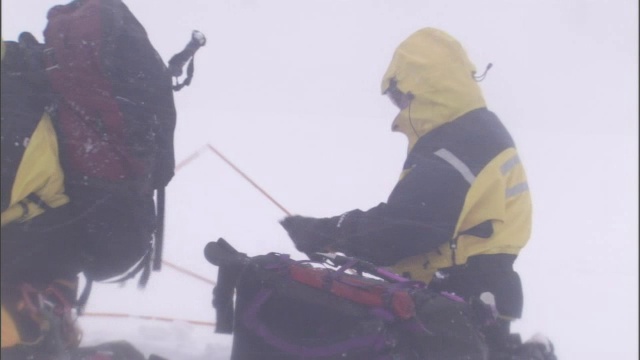 在暴风雪中，穿着冬季装备的徒步旅行者把帐篷打包好。视频素材