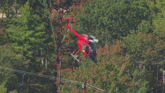 WS TS AERIAL POV红色直升机飞过森林/梅里马克县的电线，新罕布什尔州，美国视频素材