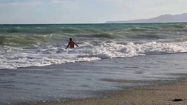 男人沿着海滩跑进海浪里视频素材