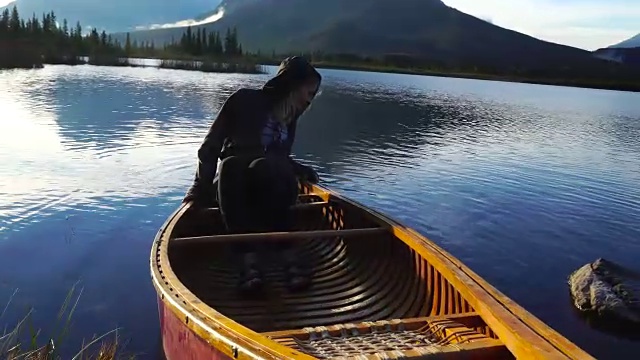 年轻女子在山间湖上的独木舟上休息视频素材