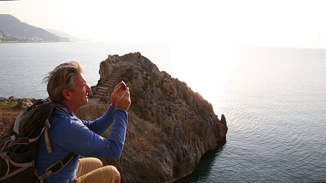 一名男性徒步旅行者在海岸线上的悬崖上停下来，眺望海面上的日出视频素材