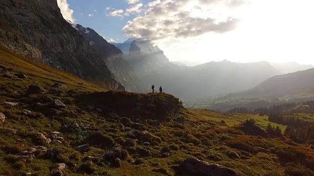 从空中(无人机)拍摄的徒步旅行者在日落时分攀登高山草甸视频素材