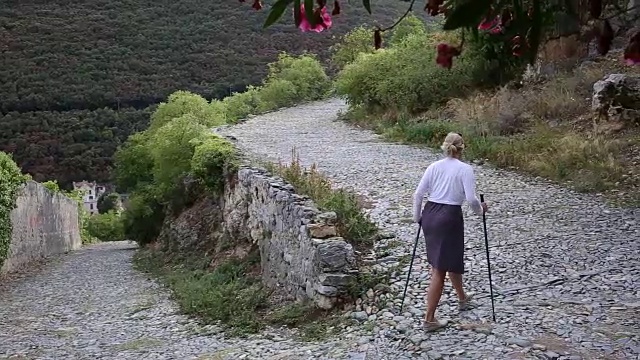 一名女子拄着登山杖，沿着鹅卵石走廊行走视频素材