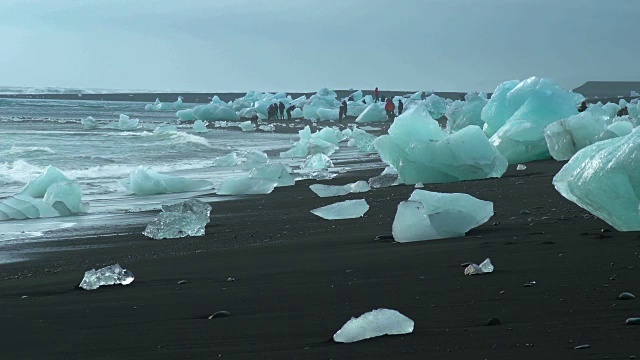 在冰岛南部Jokulsarlon泻湖附近的海滩上，游客们走在冰面上视频素材