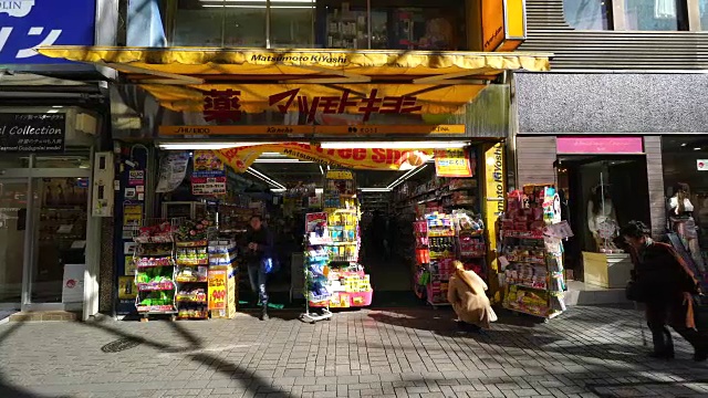 人们穿过在东京新宿莫阿2-板巷街药店的前面。视频素材