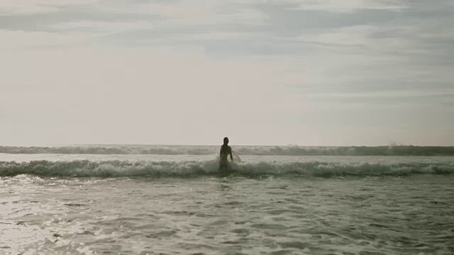 美丽的女性冲浪者穿着比基尼走进大西洋在夏天荒芜的海滩，拉冲浪板，在海浪下潜水视频素材