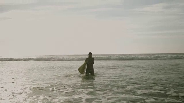 美丽的女性冲浪者穿着比基尼走出大西洋海浪在夏天荒芜的海滩，携带冲浪板视频素材