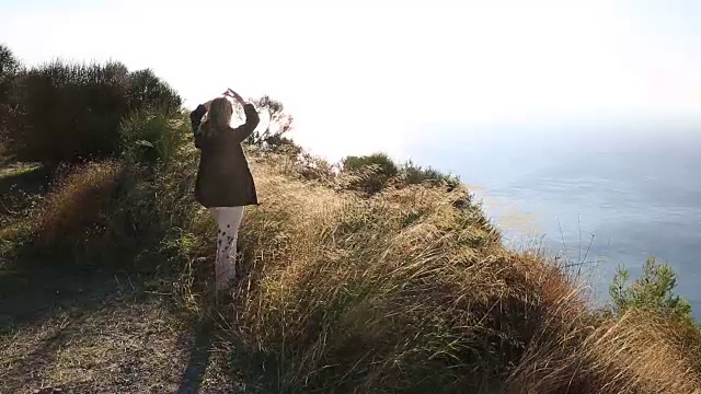 女人沿着长满草的悬崖俯瞰大海视频素材