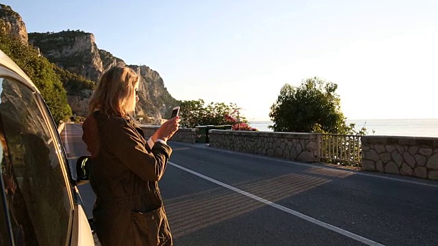 女人用智能手机拍照，从汽车和道路，大海视频素材