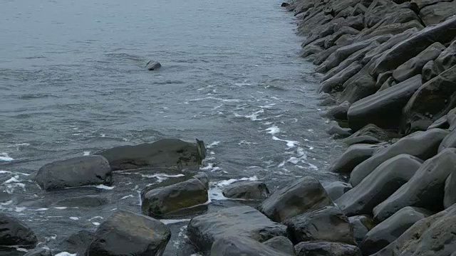 在多塞特海岸的海滩上，倾斜的海浪滚向巨石。视频素材