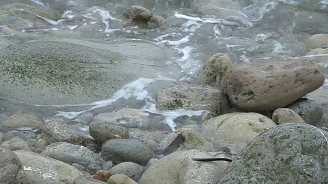 海浪滚过岩石和鹅卵石的近景。视频素材