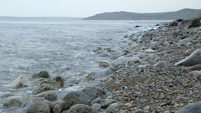 低角度拍摄的海浪滚到卵石海滩多塞特海岸。视频素材