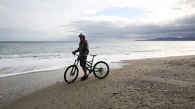 骑山地车的人在空旷的海滩上推着自行车，望着大海视频素材