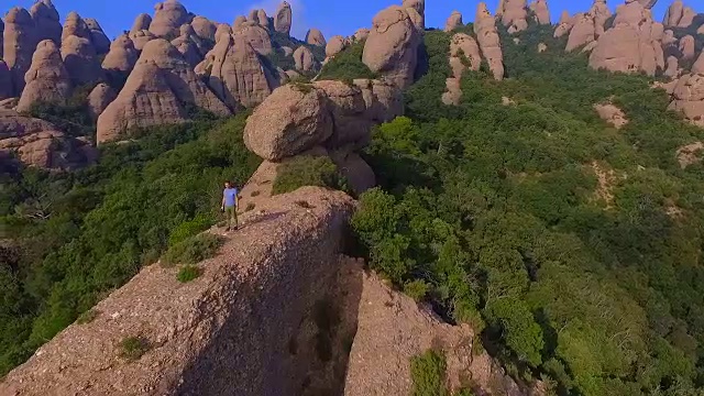 用无人机拍摄的航拍镜头，一个人在山顶沉思并拍摄蒙特塞拉特山脉的风景，他美丽而独特的构成在加泰罗尼亚地区。视频素材