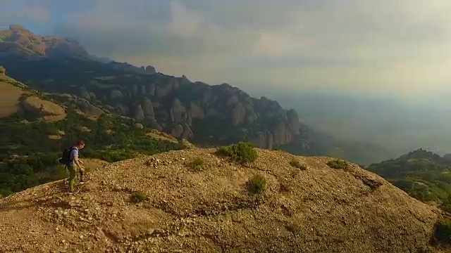 用无人机拍摄的航拍镜头，一个人在山顶沉思并拍摄蒙特塞拉特山脉的风景，他美丽而独特的构成在加泰罗尼亚地区。视频素材