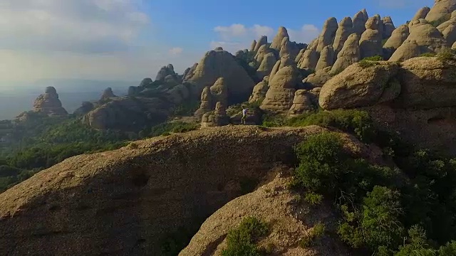 用无人机拍摄的航拍镜头，一个人在山顶沉思并拍摄蒙特塞拉特山脉的风景，他美丽而独特的构成在加泰罗尼亚地区。视频素材