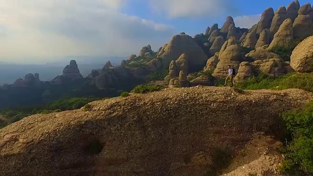 用无人机拍摄的航拍镜头，一个人在山顶沉思并拍摄蒙特塞拉特山脉的风景，他美丽而独特的构成在加泰罗尼亚地区。视频素材