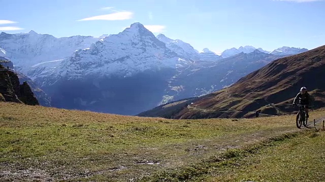 山地自行车攀登草地小径，雪山覆盖视频素材