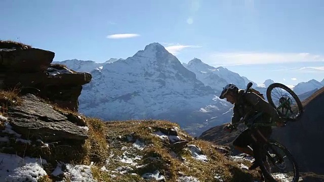 骑山地车的人爬上草地和雪山视频素材