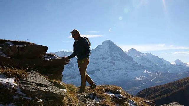 男性徒步旅行者攀登草地和雪山之上的山脊视频素材