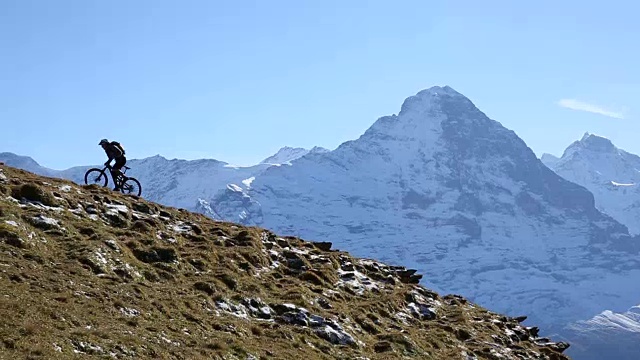 骑山地车的人爬上草地和雪山视频素材