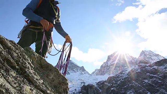 一个登山运动员从山谷上方的岩尖上抛下绳索，作绳降(滑降)。视频素材