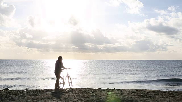 一名男子沿着海滩推着自行车，望着大海视频素材