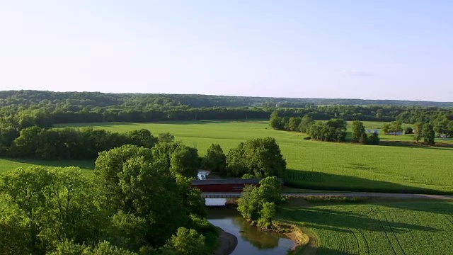 WS AERIAL POV Thorpe Ford Covered Bridge over river，农田和森林区域背景/ Parke County, Rosedale, Indiana, United States视频素材