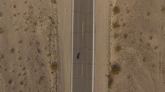 从空中俯瞰，骑自行车的人沿着空旷的道路穿过沙漠视频素材