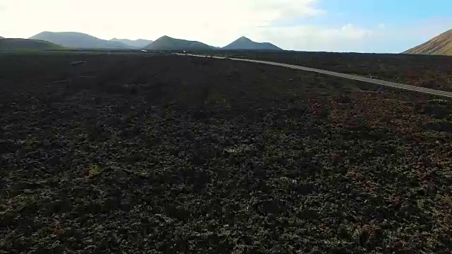 无人机在兰萨罗特岛上空拍摄的航拍画面，岛上有令人惊叹的火山景观和黑土地上漂亮的狭长直路。4 k UHD。视频素材