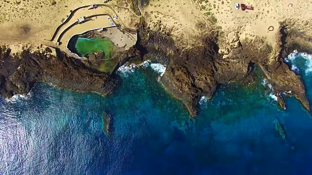 无人机在兰萨罗特火山岛上空拍摄的航拍镜头，海岸线上美丽的蓝色海水和绿色的池塘。4 k UHD。视频素材