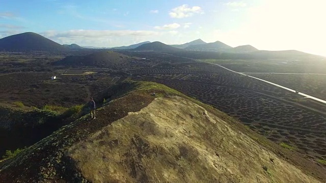 在兰萨罗特岛的火山山顶上，一个人在沉思并拍摄令人惊叹的火山景观。4 k UHD。视频素材