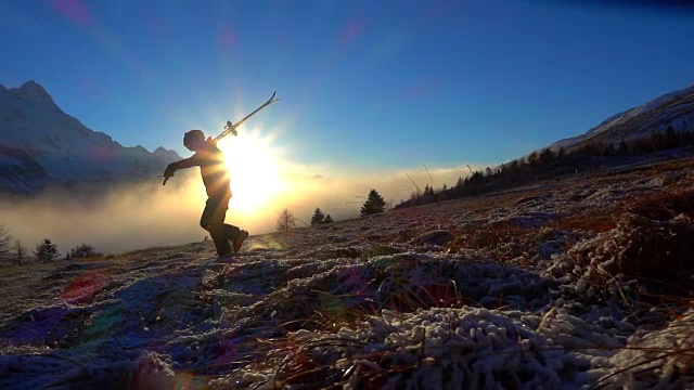 夕阳西下的雪山上，一个带着滑雪板的男人在行走视频素材