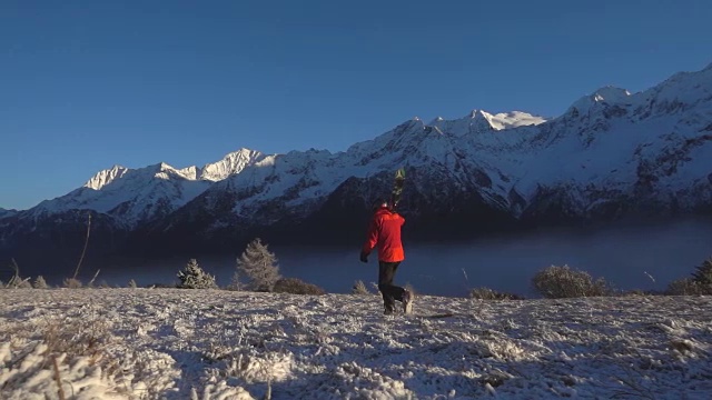 夕阳西下的雪山上，一个带着滑雪板的男人在行走视频素材