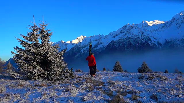 夕阳西下的雪山上，一个带着滑雪板的男人在行走视频素材