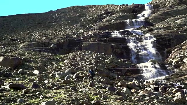 拄着拐杖在冰川岩石上行走的徒步旅行者靠近满水的地方视频素材