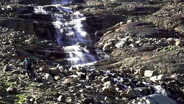 拄着拐杖在冰川岩石上行走的徒步旅行者靠近满水的地方视频素材