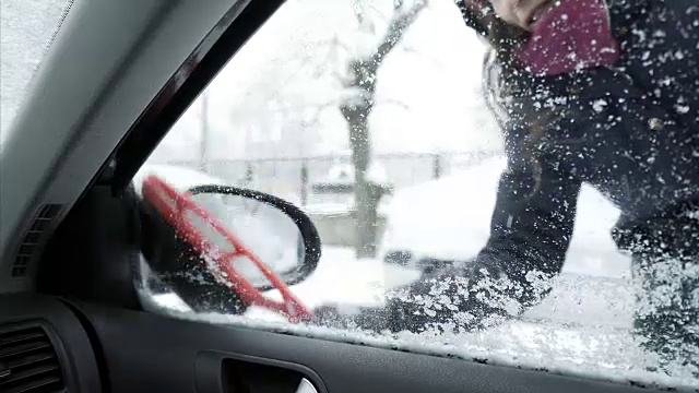 年轻女子正在清除车窗和镜子上的雪。视频素材